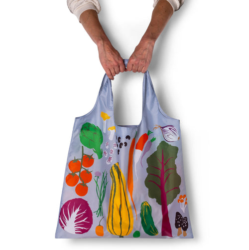 Person holding periwinkle illustrated farmers market tote bag with bold colorful vegetable print by Yellow Owl Workshop