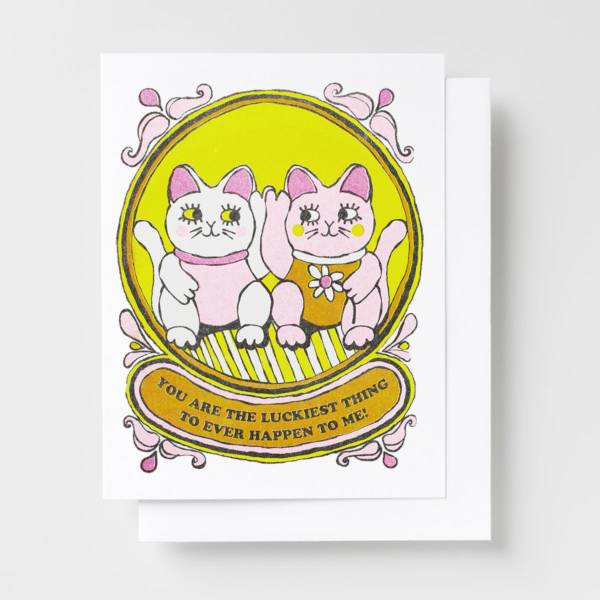 Risograph greeting card with two illustrated lucky cat characters sitting together in an ornate golden oval frame, text reads You Are the Luckiest Thing to Ever Happen to Me on a gold banner
