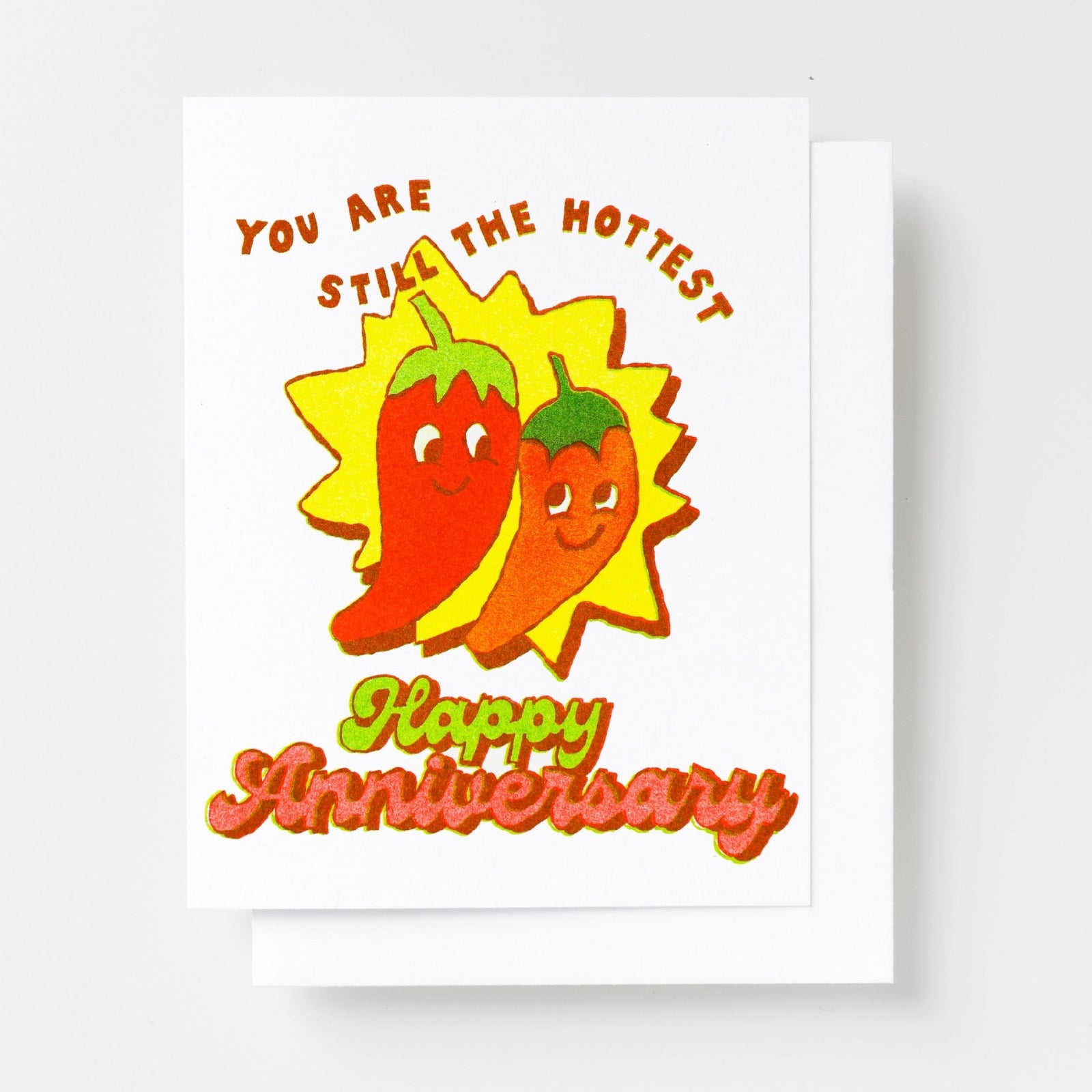 Risograph greeting card with two smiling chili pepper characters on a yellow starburst, text reads You Are Still the Hottest Happy Anniversary in red and green lettering